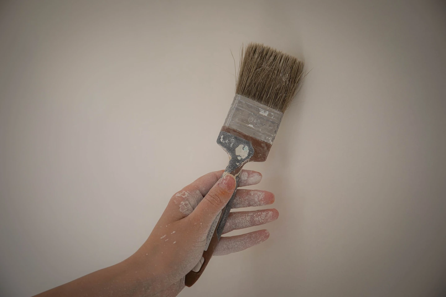 Main tenant un pinceau contre un mur beige